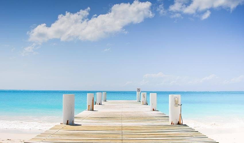 A pier leading to a beach with blue water and white sand.