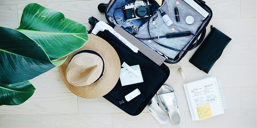 A suitcase, hat, sunglasses, and other items on a wooden floor.