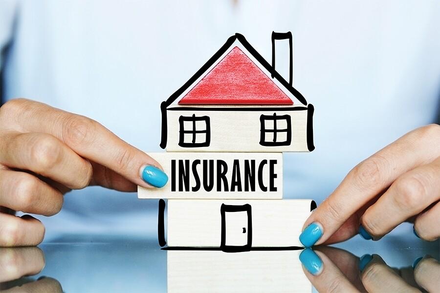 A woman holding a wooden house with the word insurance on it.