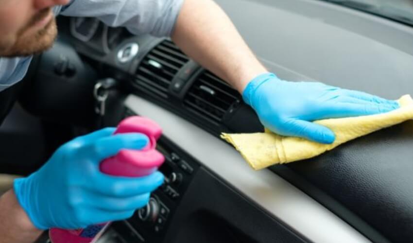 A man in blue gloves cleaning the dashboard of a car.