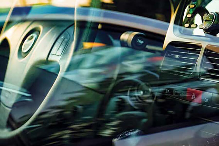 Interior view of a car through a reflective glass showing steering wheel and dashboard.
