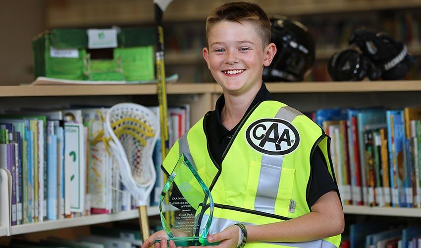 A young boy holding a lacrosse trophy in a library.
