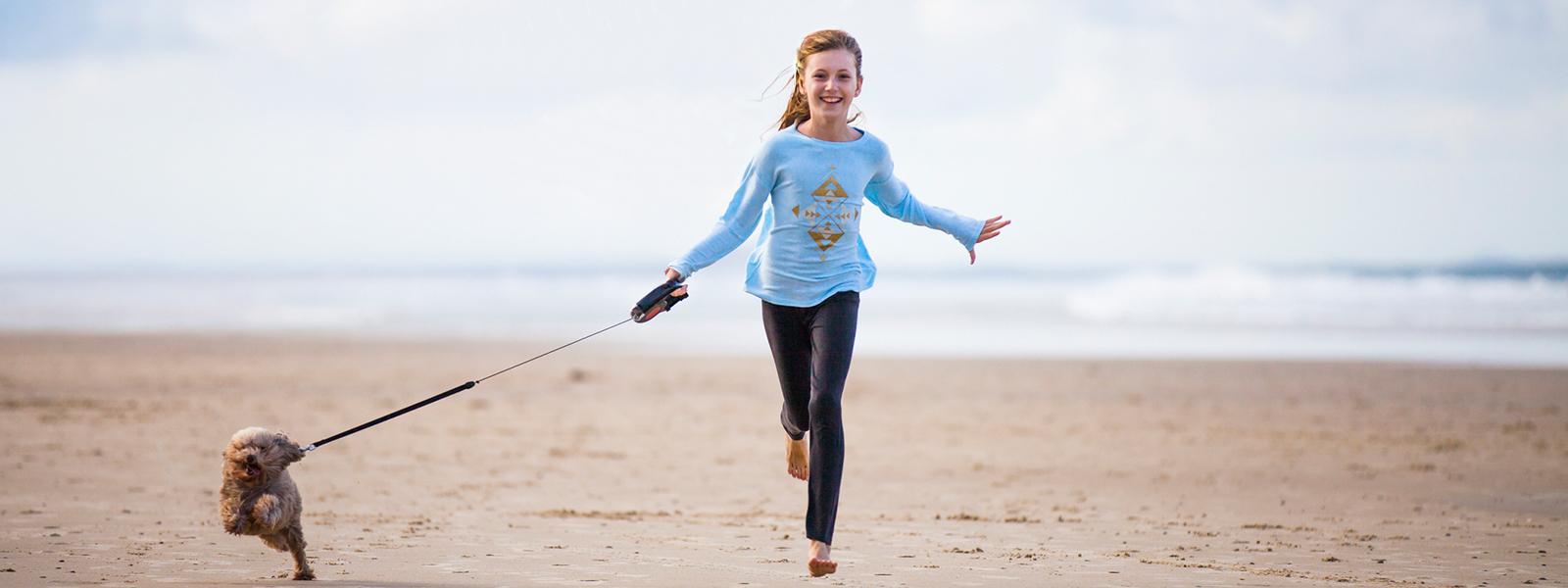 Young girl running on a beach with her small dog.