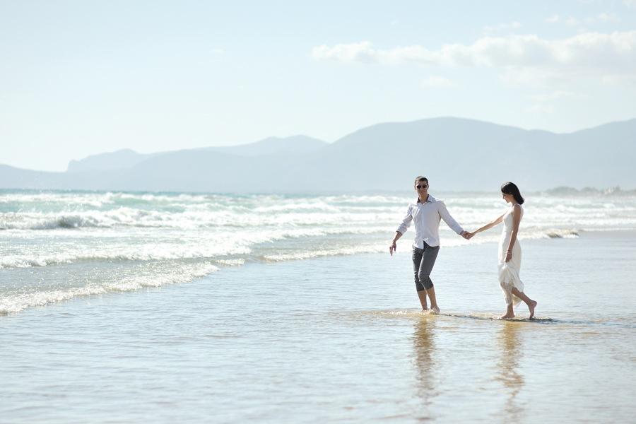 Couple holding hands and walking along the shoreline at the beach.