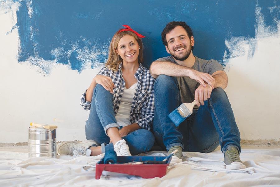 A couple sitting on the floor painting a blue wall.