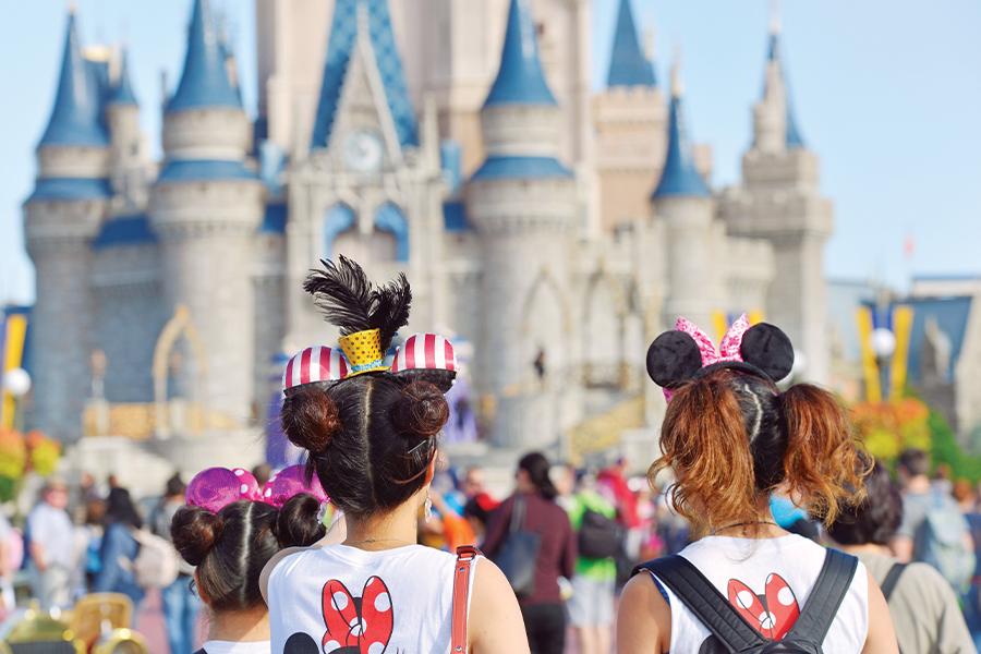 Two girls wearing mickey mouse ears in front of cinderella castle.