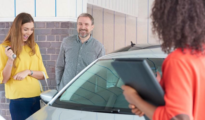 A man and woman are looking at a car in a dealership.