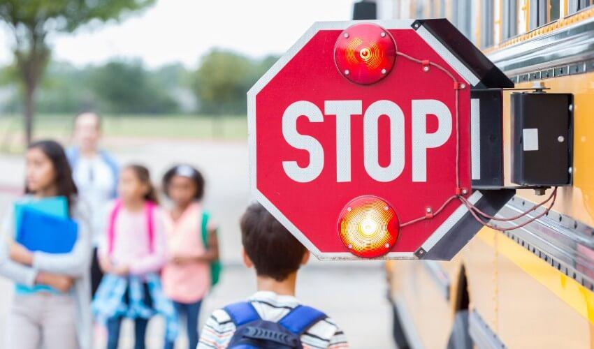 A group of children standing in front of a stop sign on a school bus.
