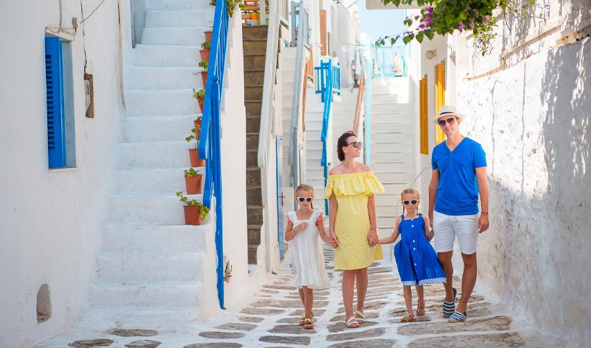 A family walking through a picturesque alley with white-washed walls and blue doors, typical of a greek island setting.