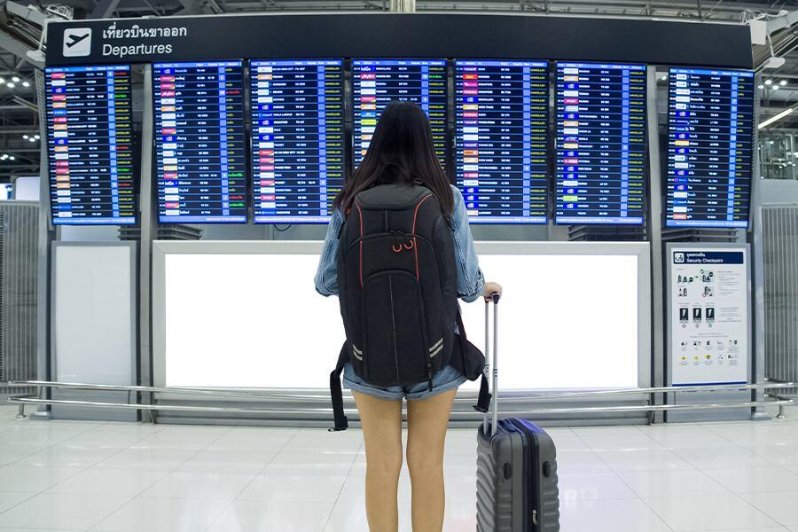 A woman with a backpack in front of an airport terminal.