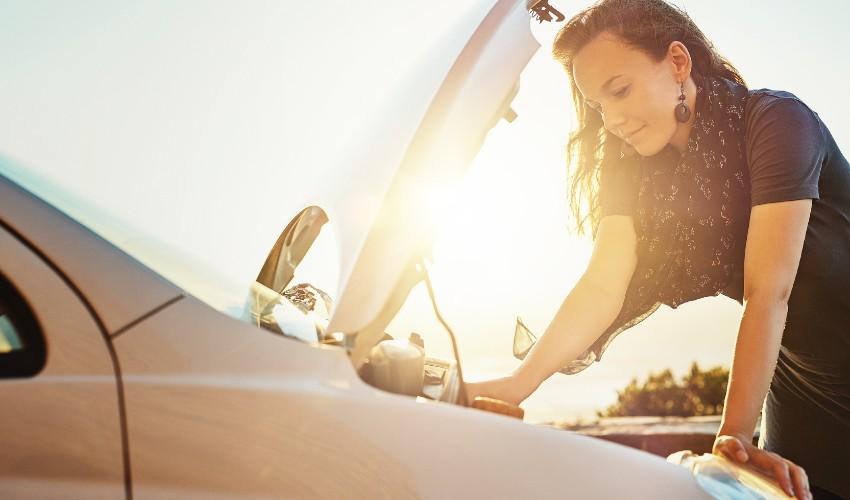 A woman looking at the hood of a car.