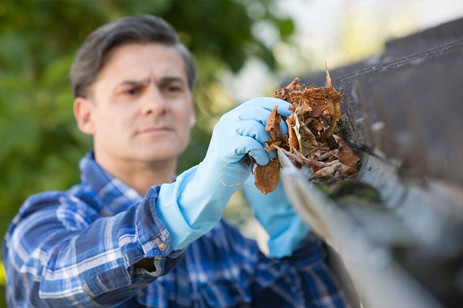 A man cleaning gutters with gloves on.