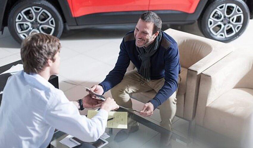 A man is talking to a man in a car showroom.