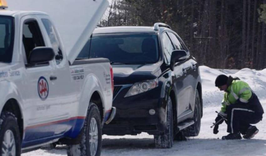 A man is repairing a car on a snowy road.