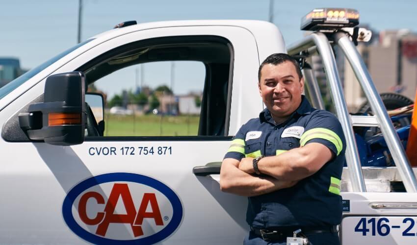 A roadside assistance technician leaning against a caa service vehicle.