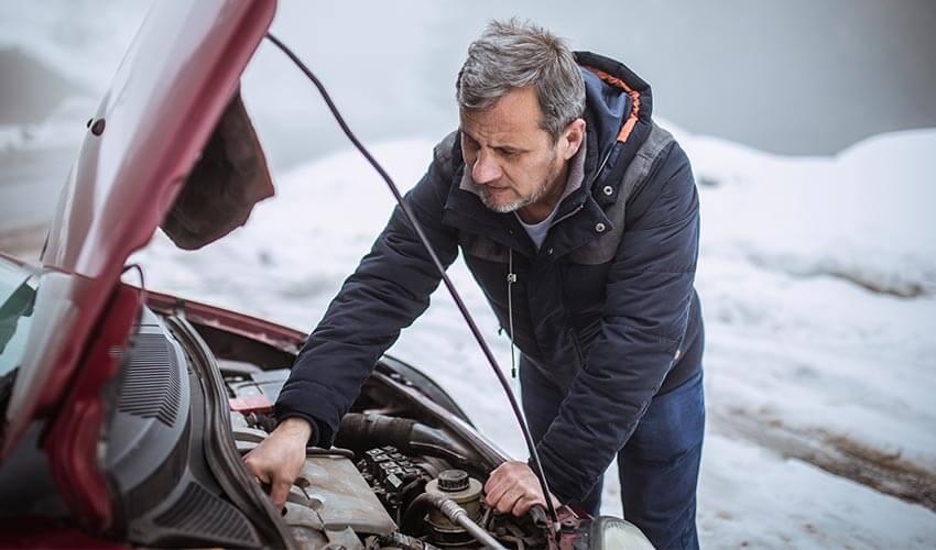 A man is working on his car in the snow.