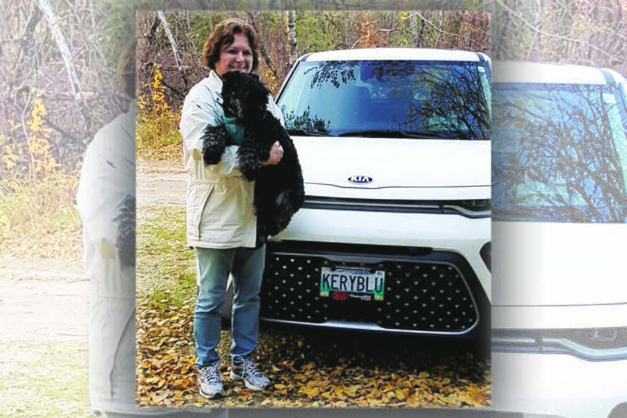 A woman holding a dog in front of a white suv.