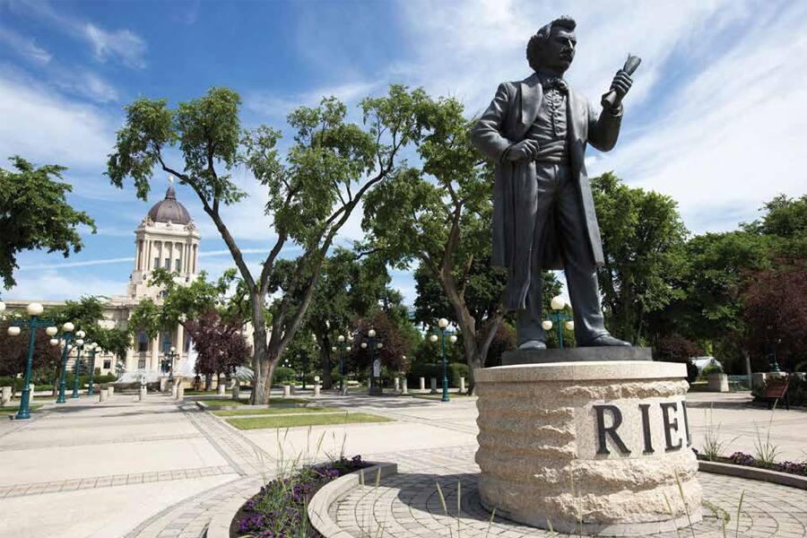 Statue of a historical figure in a park with a government building in the background.