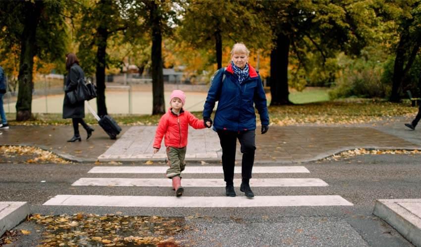 A woman and a child crossing a crosswalk in a park.