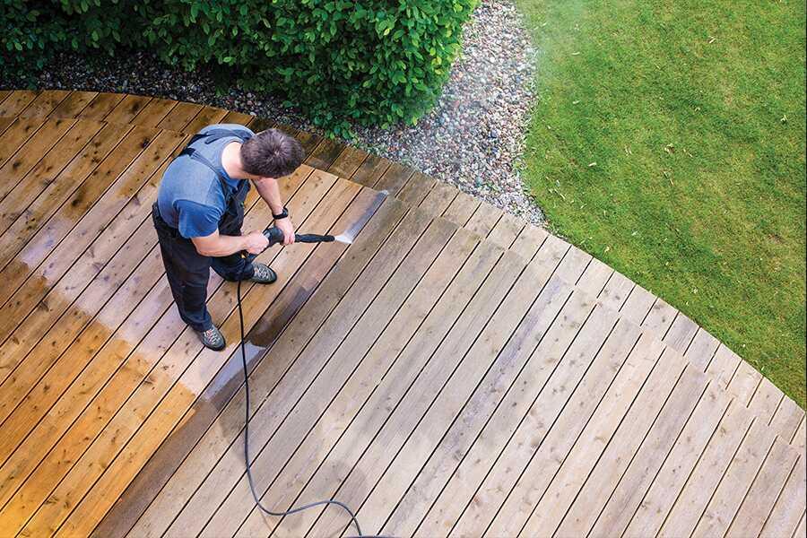 A man cleaning a wooden deck with a pressure washer.