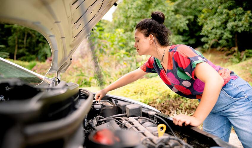 A woman inspecting the hood of a car.