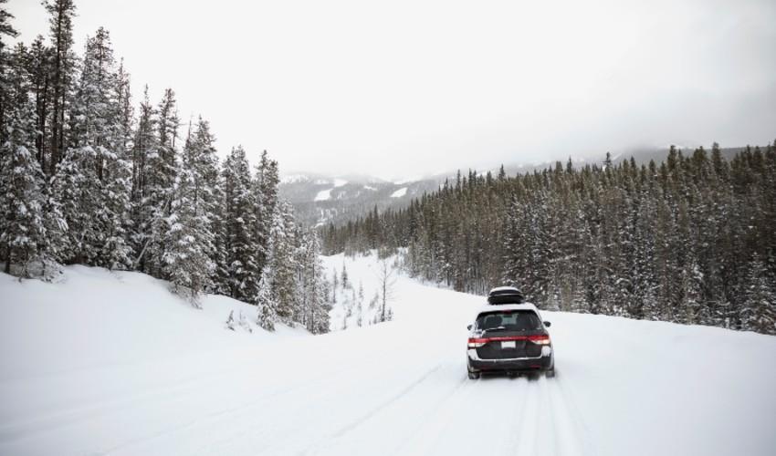 A suv driving down a snowy road with trees in the background.