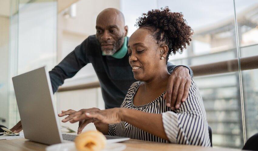 A man and woman working on a laptop in an office.