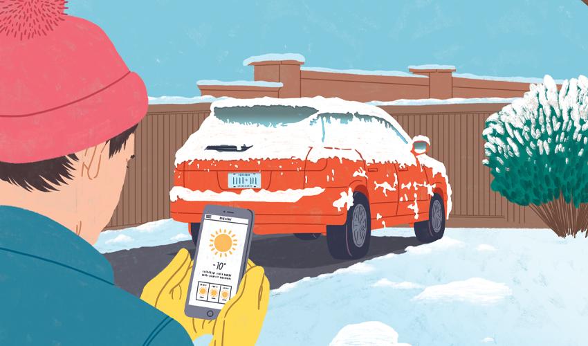 A person holding a phone with a snow covered car in the driveway.