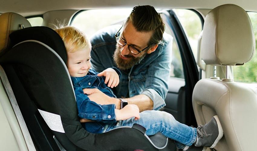A man is holding a child in a car seat.