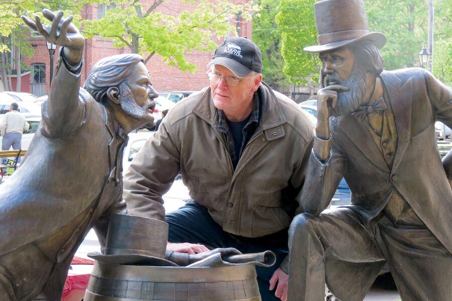 A man kneeling next to a statue of three men.