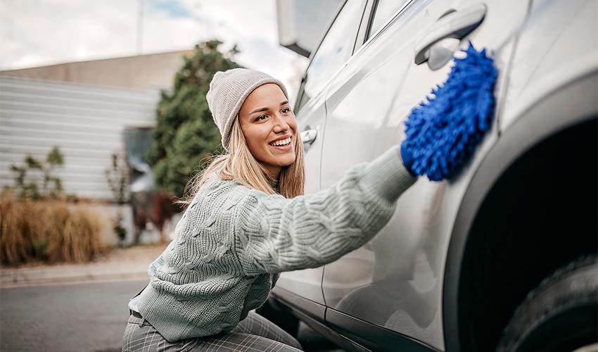 A woman cleaning her car with a blue mop.