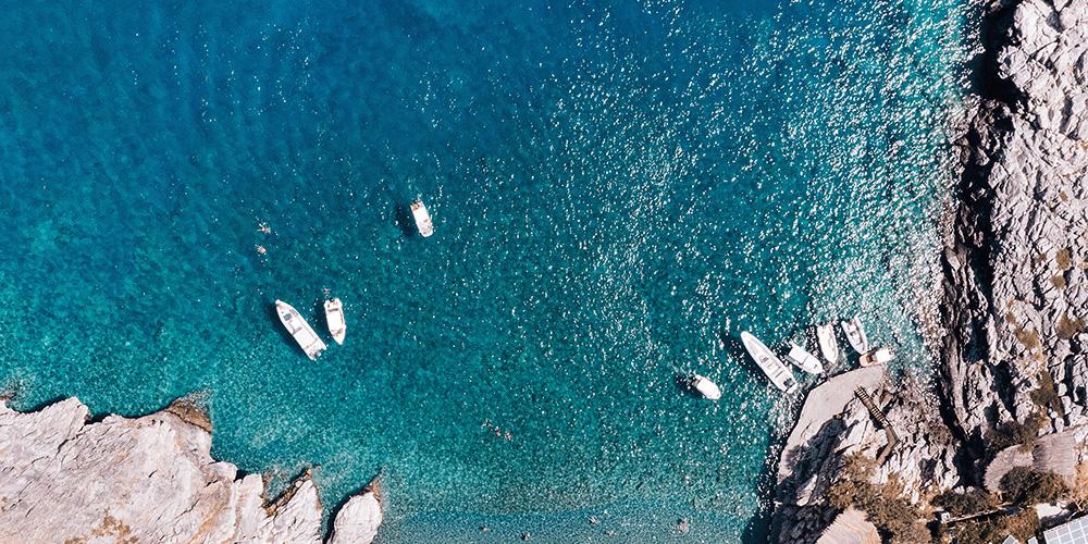A group of boats in the water near a rocky shore.