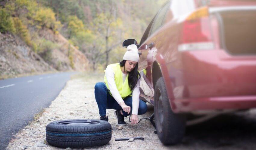 A woman fixing a tire on the side of the road.