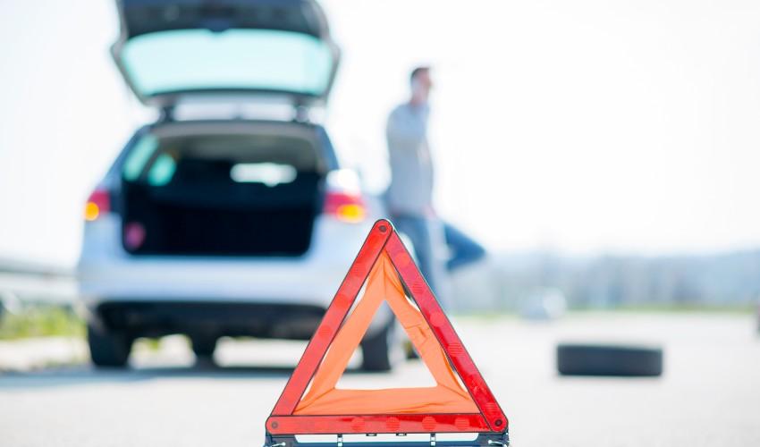 A man standing next to a car with a broken tire.
