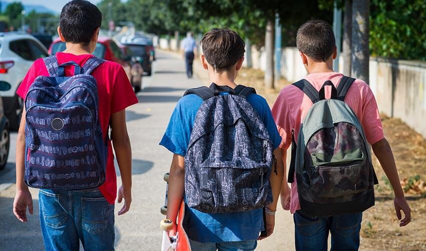 Three boys with backpacks walking down the street.
