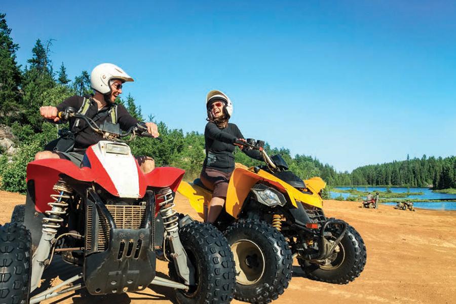 Two people riding atvs on a dirt road near a lake.
