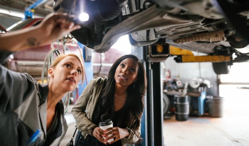 Two women working on a car in a garage.