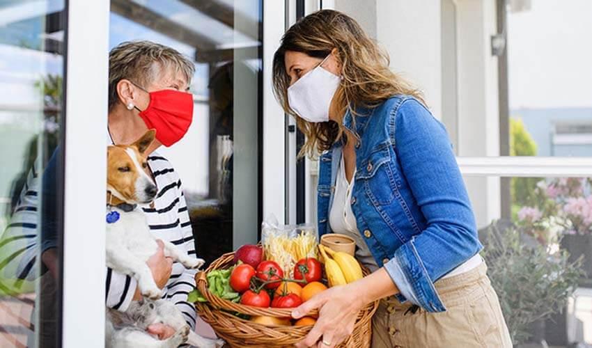 A woman wearing a face mask with a basket of fruit and a dog.