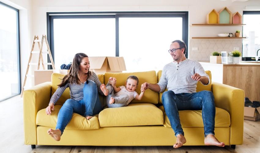 A family sits on a yellow couch in their new home.