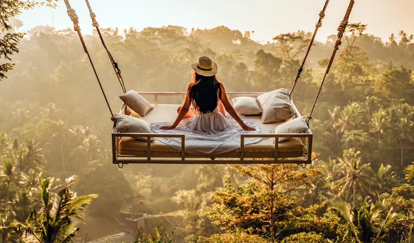A woman sitting on a swing in the jungle.