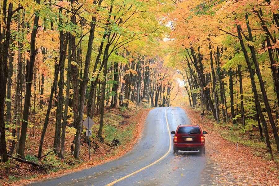 A red car driving down a road in the fall.
